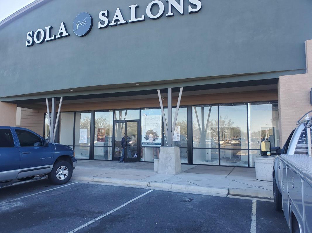 Exterior of Sola Salons commercial building with modern window tinting, reflecting parking lot, cars, and blue sky, enhancing privacy, glare reduction, and aesthetic appeal.
